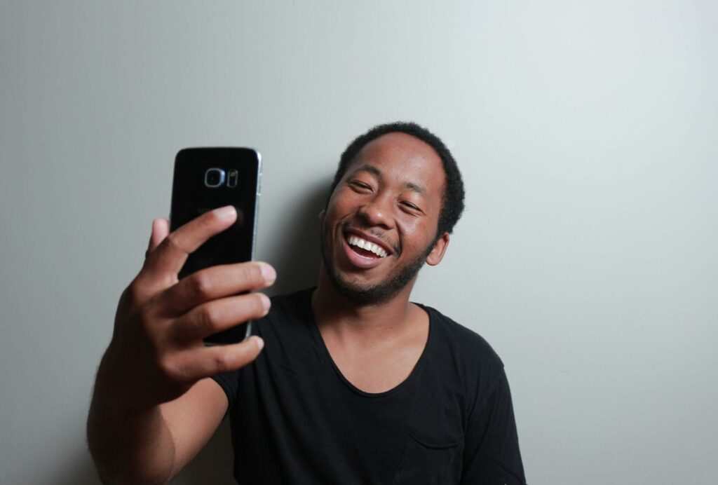 man smiling at his smartphone selfie laughing