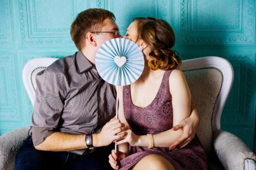 man and woman kissing behind fan with a heart print