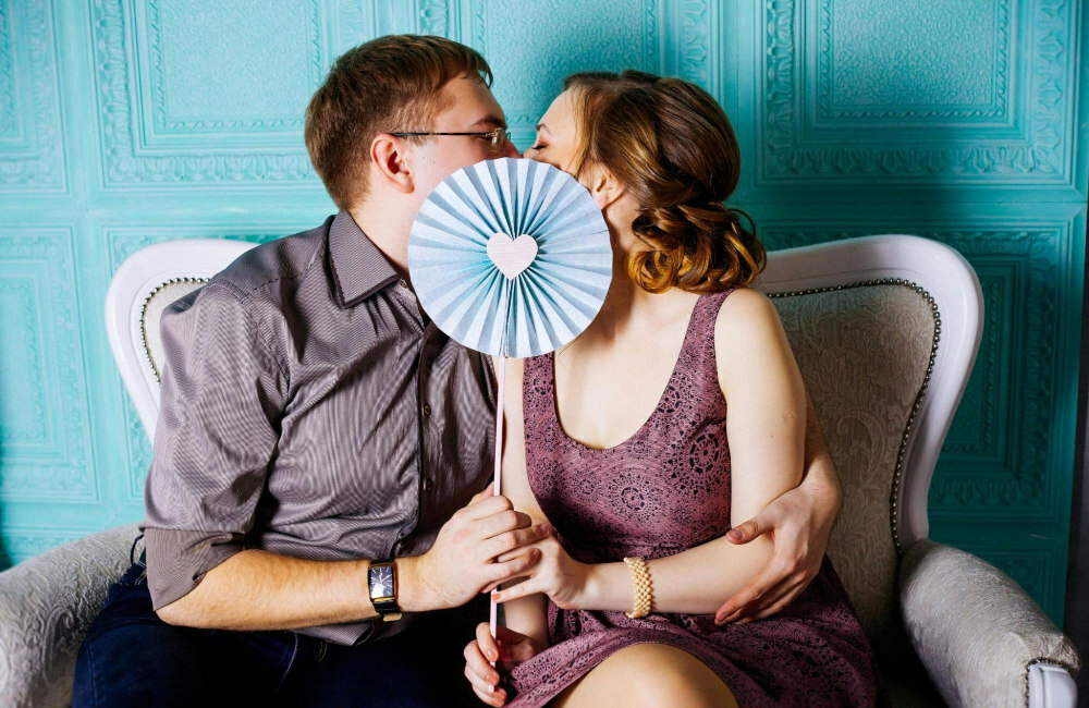 man and woman kissing behind fan with a heart print