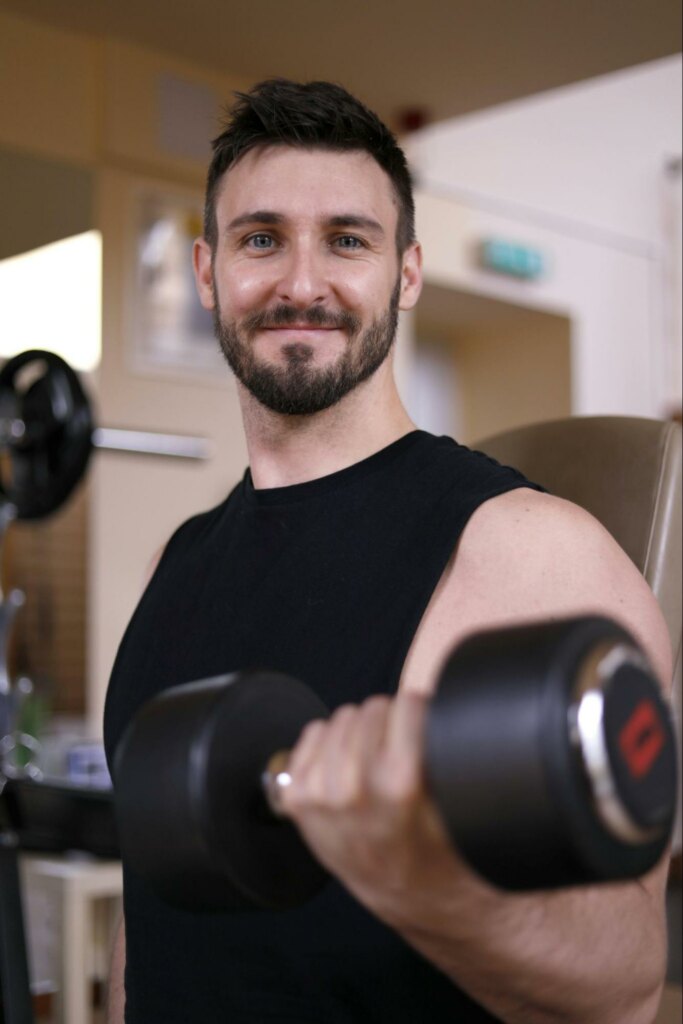 man smiling at the camera while lifting weights, dating photoshoot