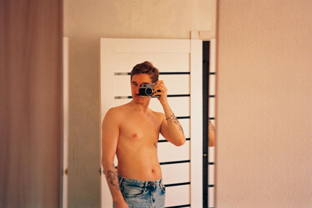 shirtless man taking a mirror selfie with camera